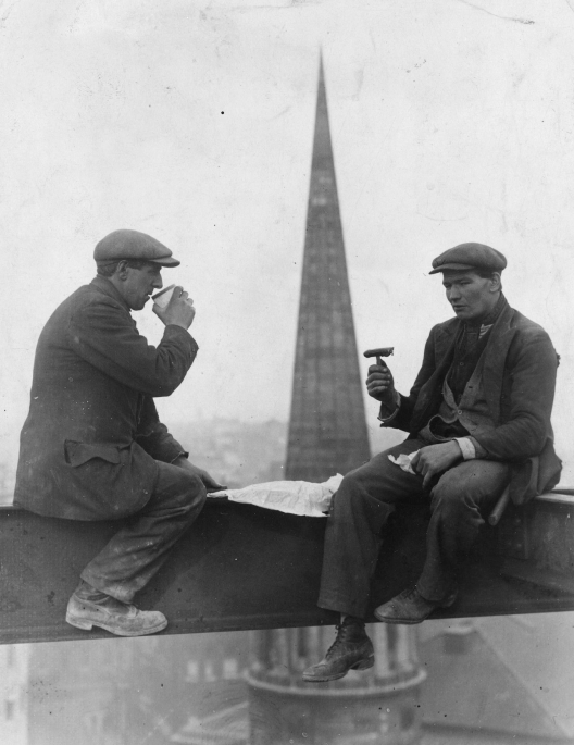 Photo ancienne en noir et blanc de deux ouvriers prenant leur casse-croûte a plusieurs dizaine de mètres hauteur sur une charpente en acier d'un building en construction.