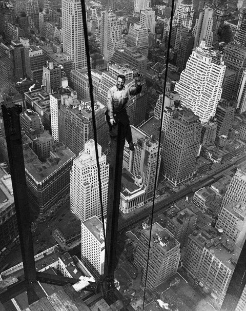 Photo des années 80 en noir et blanc d'un ouvrier marchant sur une charpente en acier d'un building en construction, sans peur de tomber dans le vide.